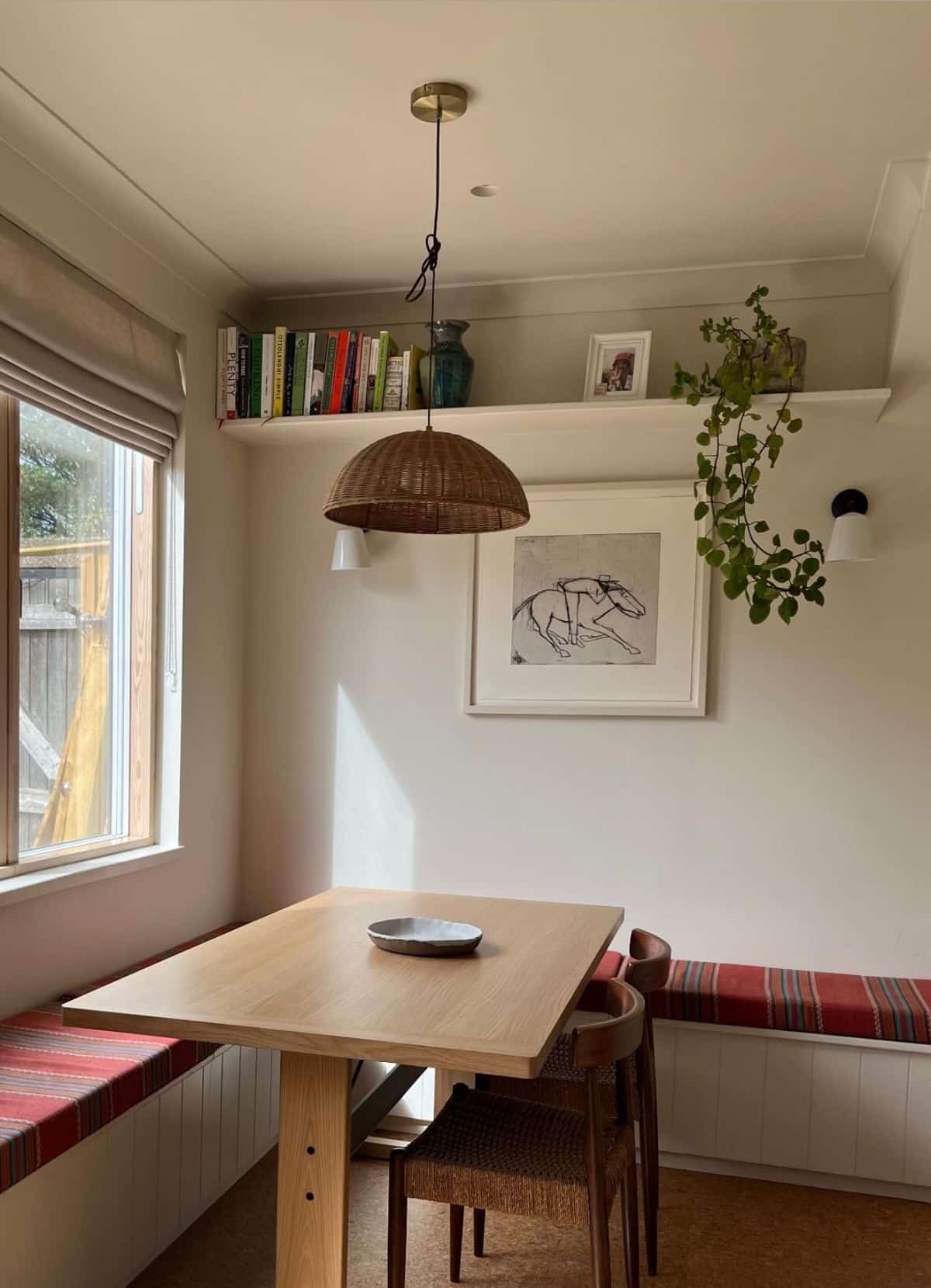 Two-sided built-in banquette with red striped cushions, a square oak table and a cookbook shelf above
