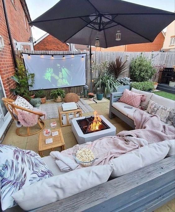 Backyard outdoor cinema with a projector screen, corner sofa, blankets, popcorn and a fire pit table