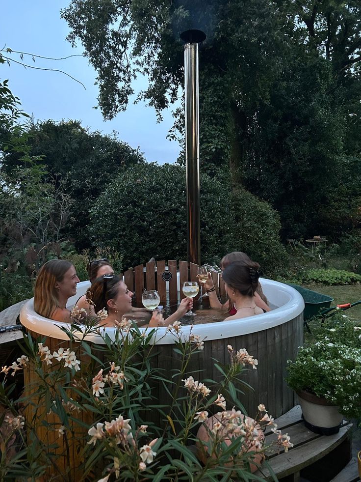 Wood-fired hot tub with a chimney in a garden at dusk, surrounded by flowering plants