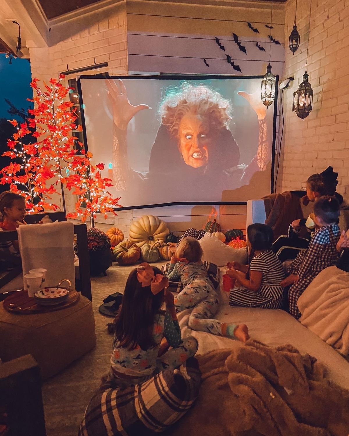 Covered porch movie den with pillows, throws, pumpkins, lanterns and a projector screen for a seasonal film