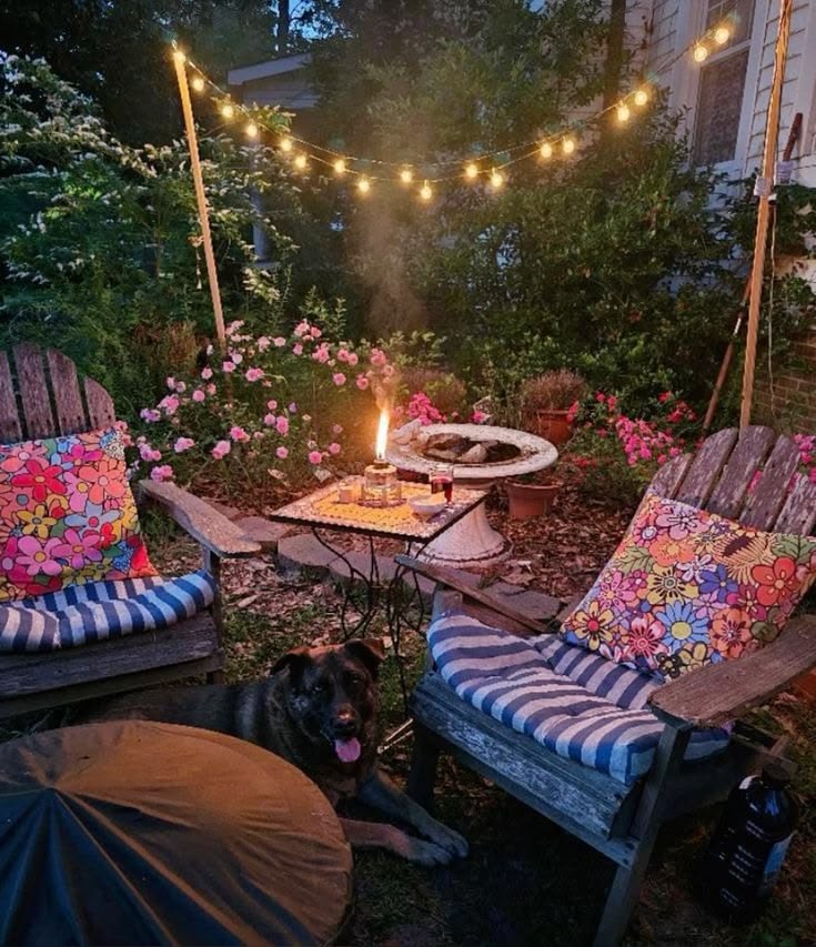 Weathered wooden Adirondack chairs with bright floral cushions beside a low fire bowl in a cottage garden