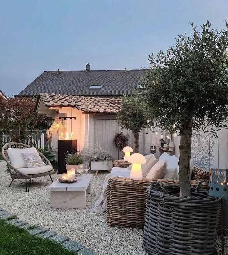 Neutral grey and cream gravel courtyard with rattan seating, a potted olive tree and glowing mushroom lamps