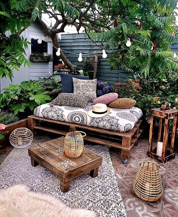 Rustic pallet daybed piled with mandala-print cushions under a tree, with woven lanterns and a patterned rug