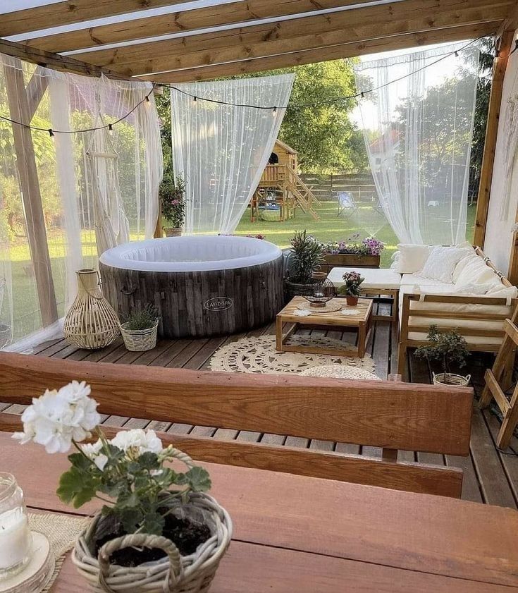 Covered deck with sheer white voile curtains around an inflatable hot tub, string lights and a doily-style rug