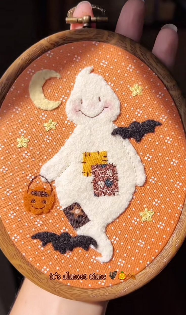 Embroidery hoop with a felt ghost, stitched stars, bats and a moon on orange fabric