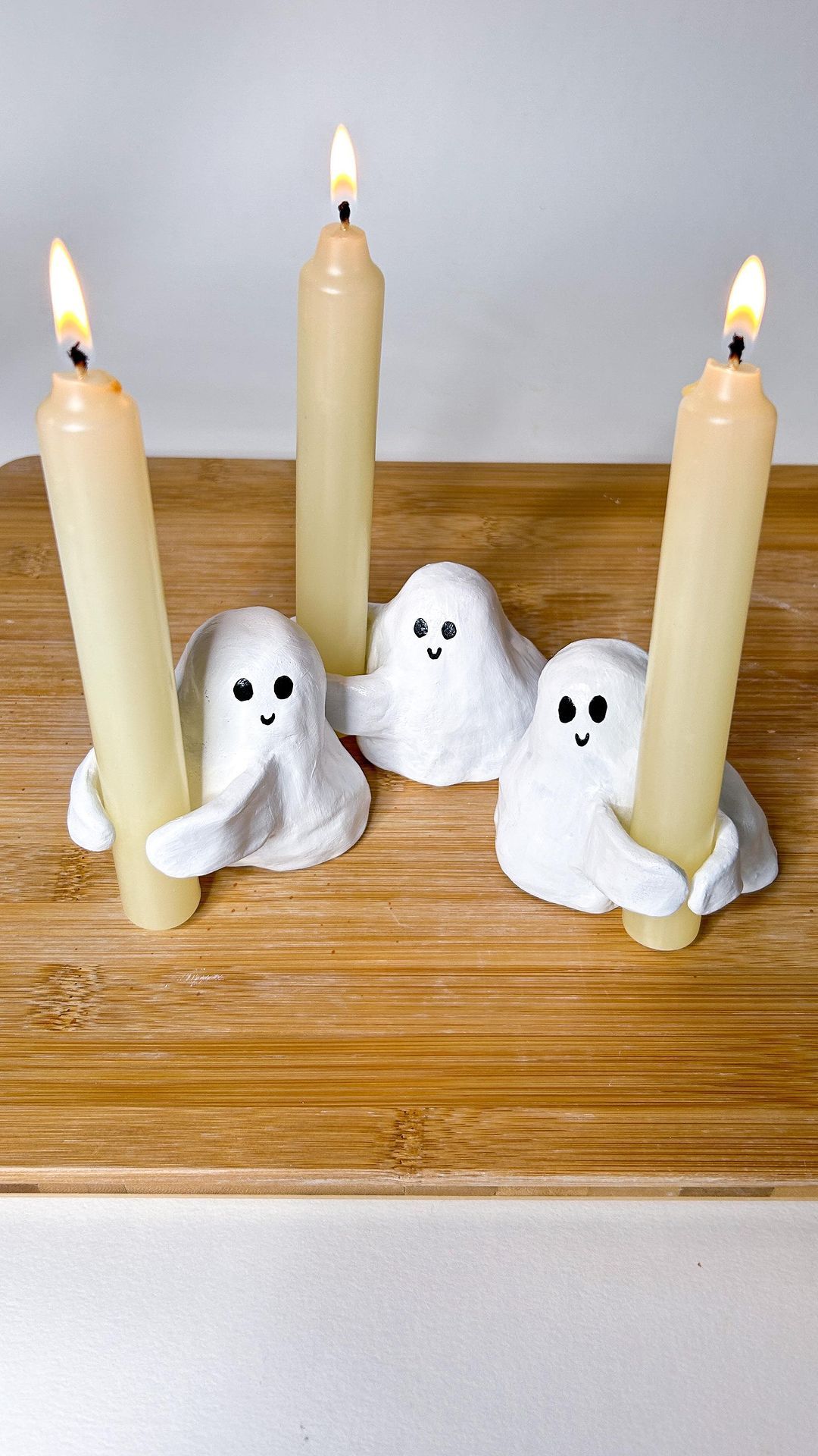 Air-dry clay ghost candle holders cradling cream taper candles on a board