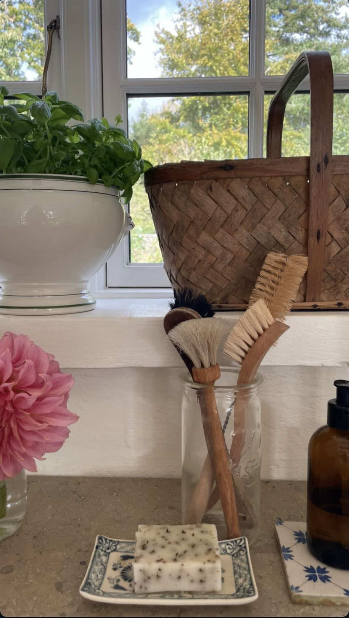 Kitchen sink soap tray idea with dish brushes in a clear glass jar and speckled soap on a blue and white patterned dish on a cottage windowsill
