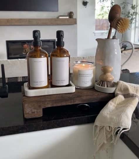 Marble tray holding matching amber hand wash and dish soap bottles with a candle and a jug of brushes