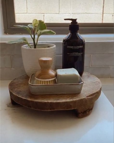 Footed wooden riser holding a ceramic tray with a soap bar and brush, an amber pump bottle and a small plant