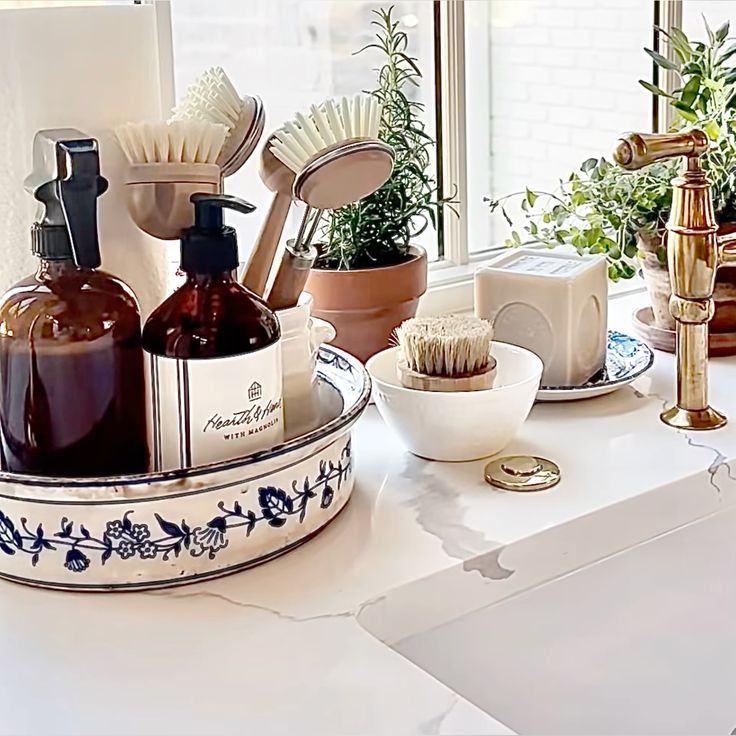 Blue and white patterned tray holding amber soap bottles and a crock of dish brushes near a window