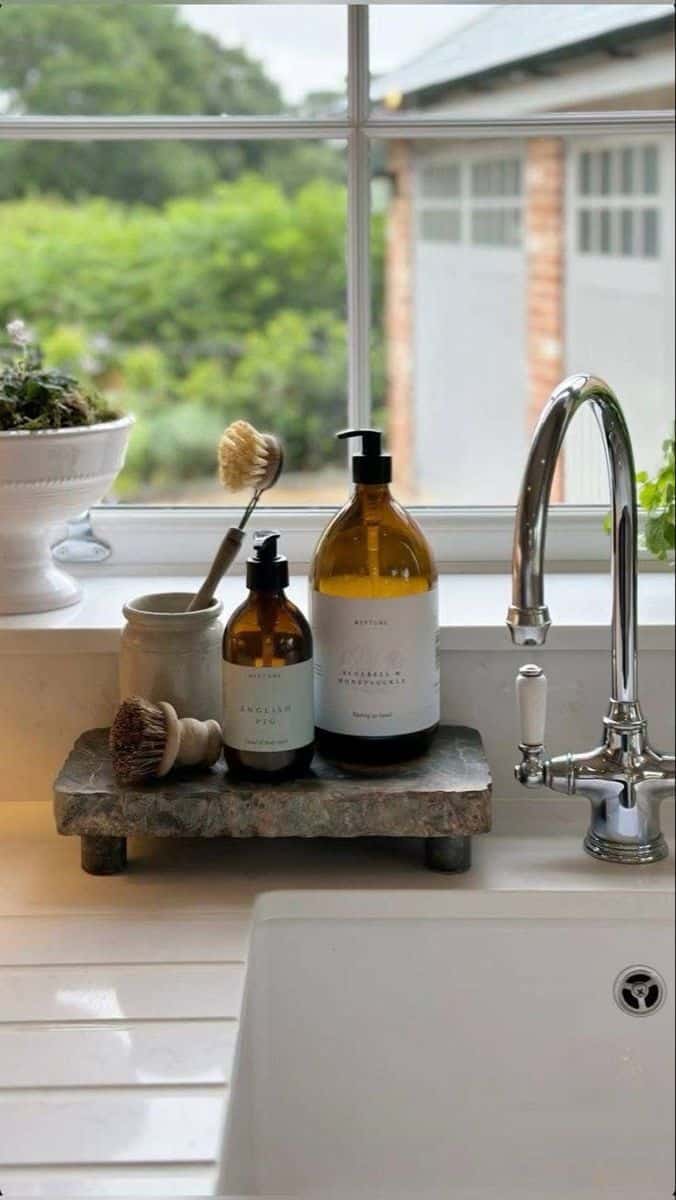 Rough cut stone riser holding amber bottles and a dish brush beside a white farmhouse sink