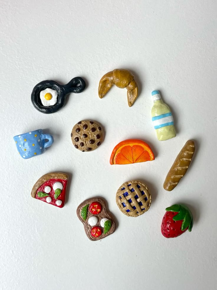 Realistic clay food magnets including a fried egg in a pan, croissant, milk bottle, cookie and pizza slice on a white background
