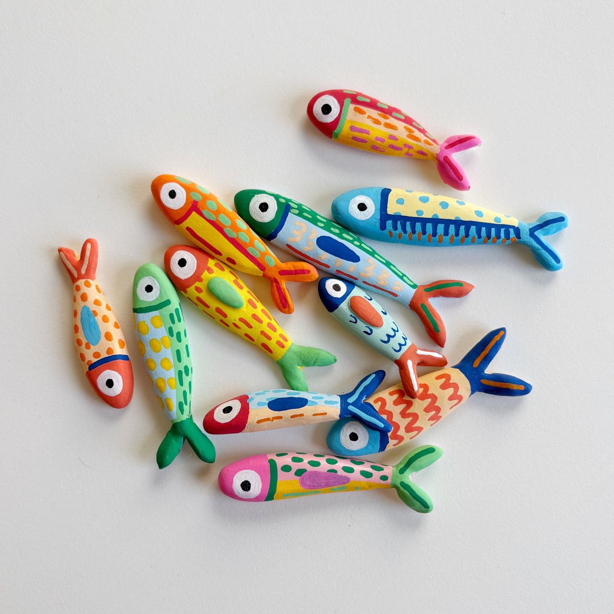 Hand-painted folk-art clay fish magnets in bright patterns of dots, dashes and stripes