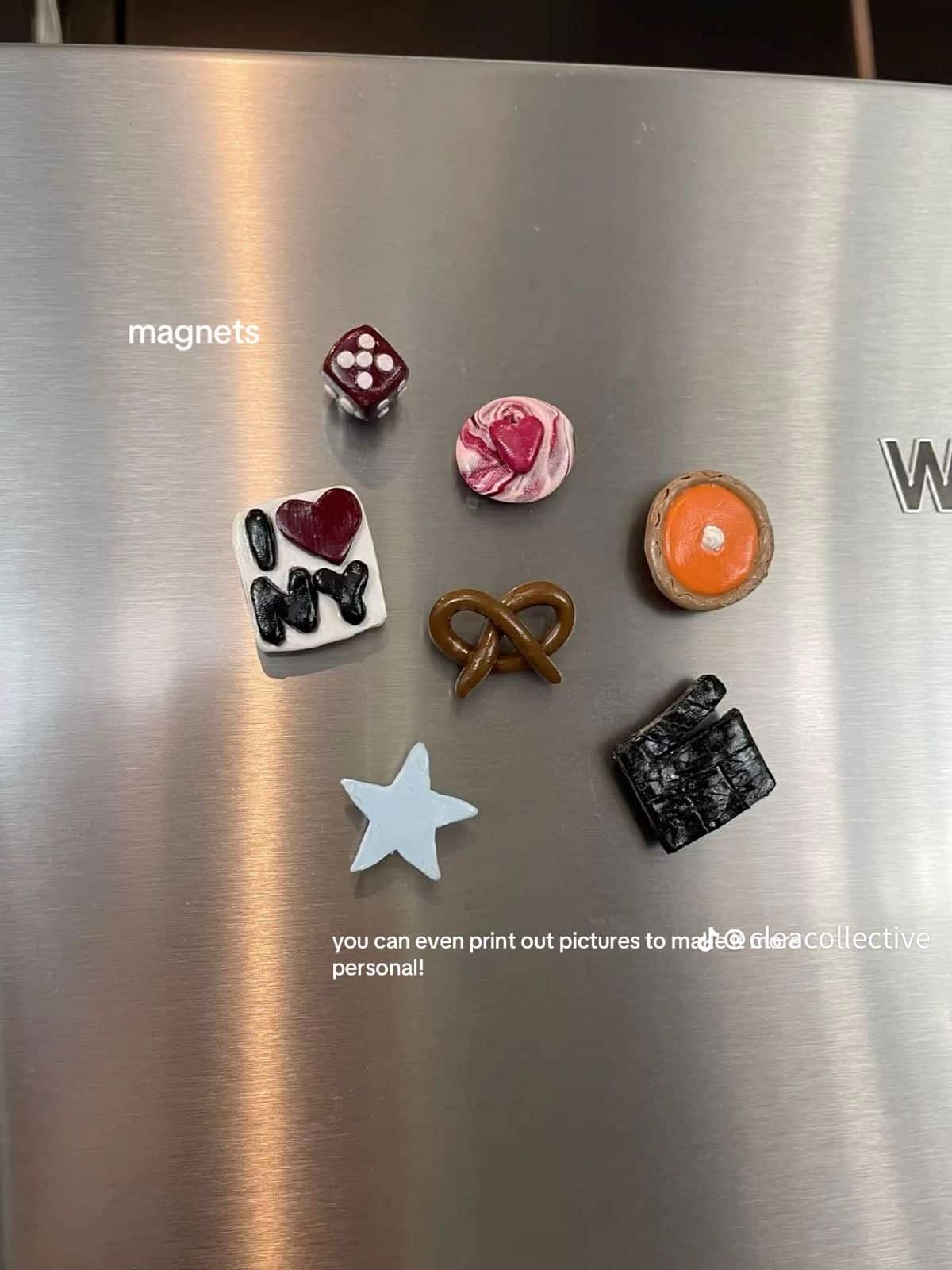 Eclectic clay magnets in moody tones including a dice, pretzel and New York tile on a stainless steel fridge