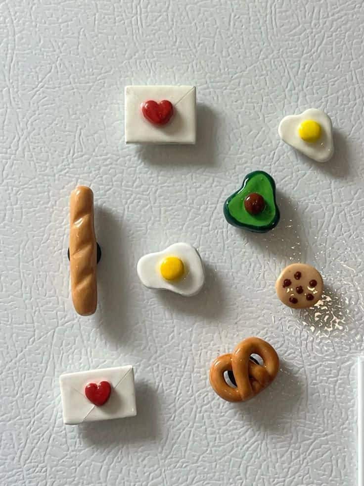 Simple realistic clay food magnets including a baguette, egg, avocado and cookie on a white fridge