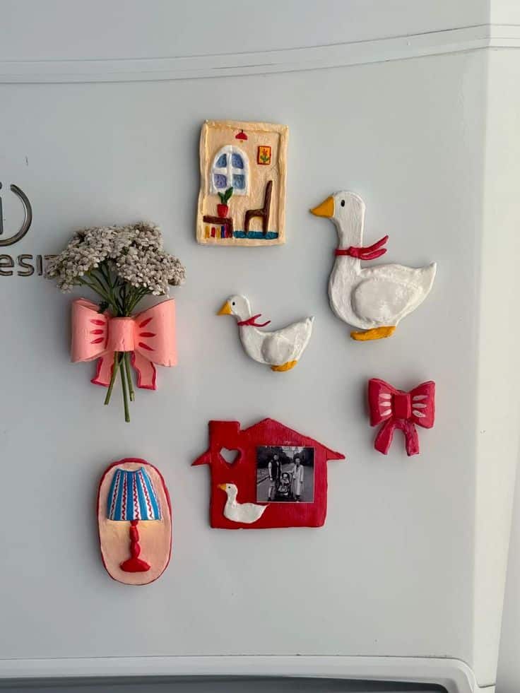 Cottagecore clay magnets including ribboned geese, a painted house and a dried-flower bouquet on a white fridge