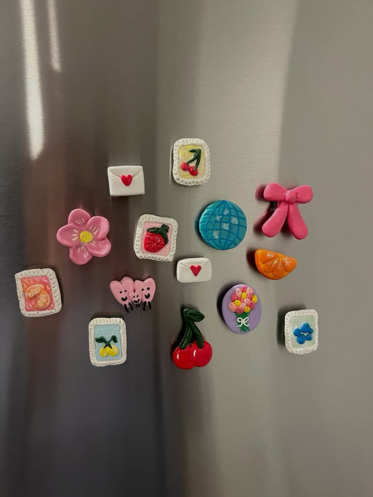 Pastel clay magnets with tiny framed fruit paintings, a bow, flower and disco ball on a stainless steel fridge