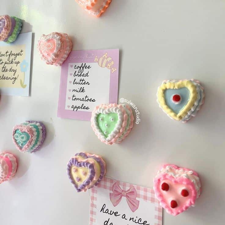Heart-shaped clay cake magnets decorated with piped pastel frosting on a white fridge
