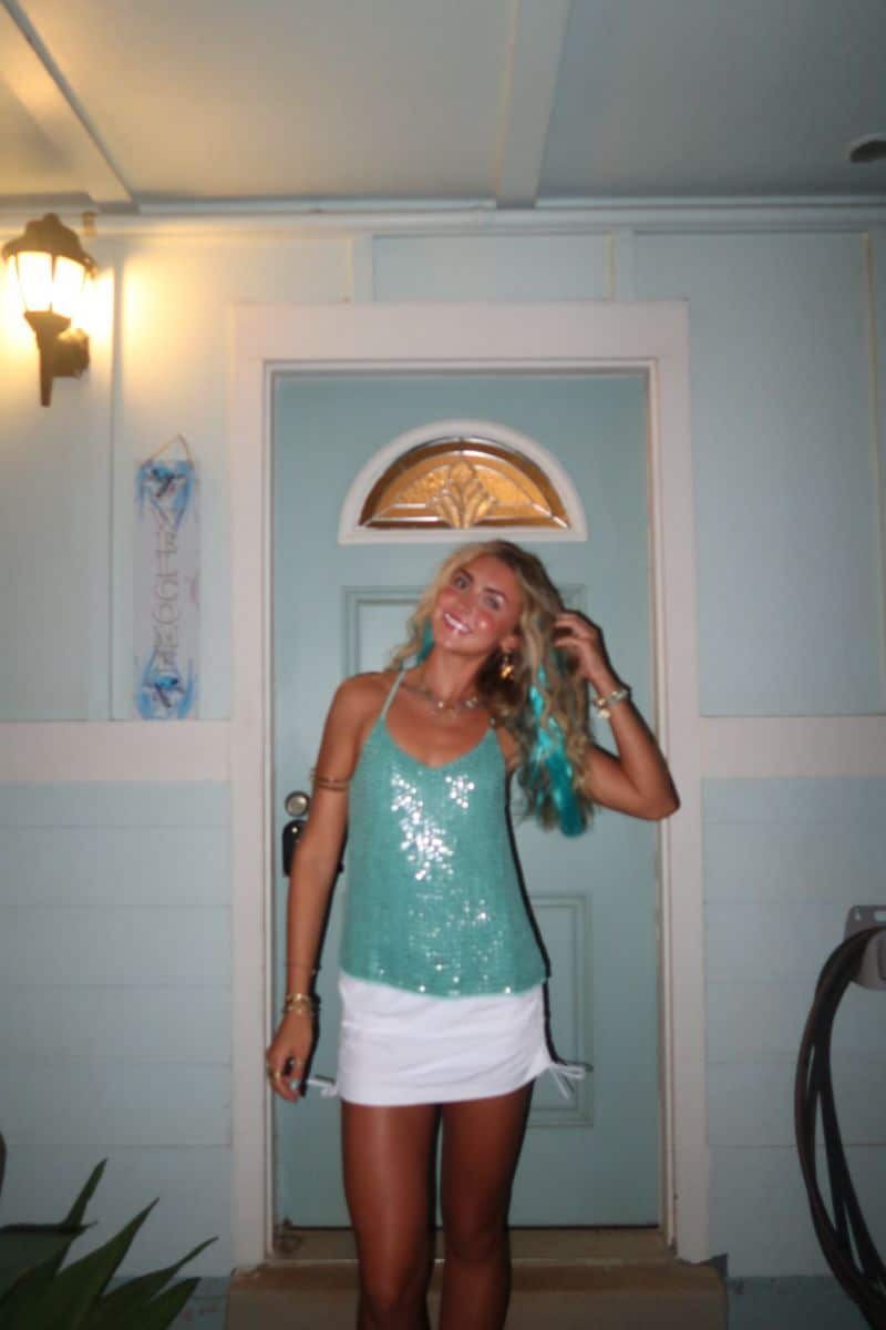 Person in a teal sequinned tank and white skort with aqua streaks in their hair, dressed as Aquamarine.