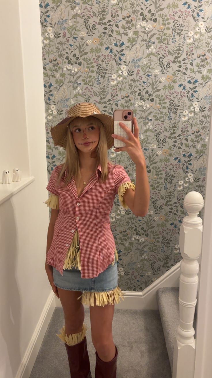 Person in a gingham shirt and denim skirt trimmed with straw, a straw hat and stitched face makeup, dressed as a scarecrow.