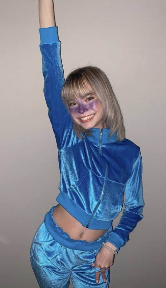 Person in an all-blue velour tracksuit with matching blue makeup, dressed as Violet Beauregarde from Charlie and the Chocolate Factory.