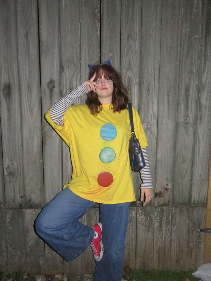 Person in an oversized yellow tee with large coloured buttons and cat ears, a striped long-sleeve top underneath, dressed as Pete the Cat.