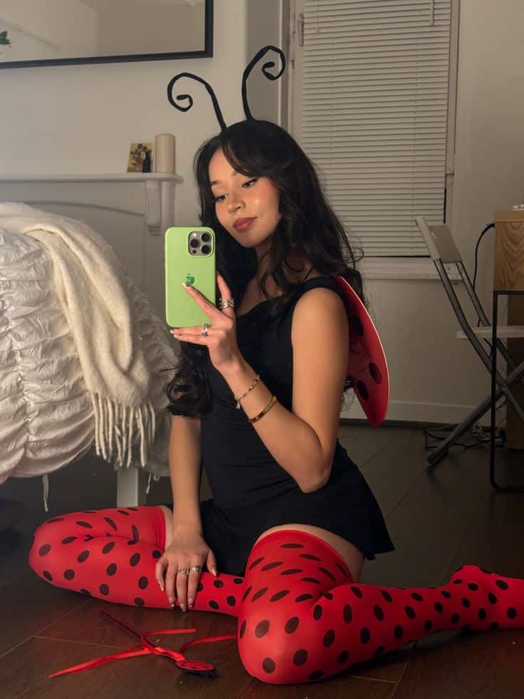Person in a black bodysuit with red polka-dot tights, wings and antennae, dressed as a ladybird.