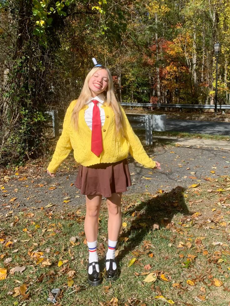 Person in a yellow cable-knit cardigan, white shirt with a red tie and brown pleated skirt, dressed as SpongeBob SquarePants.
