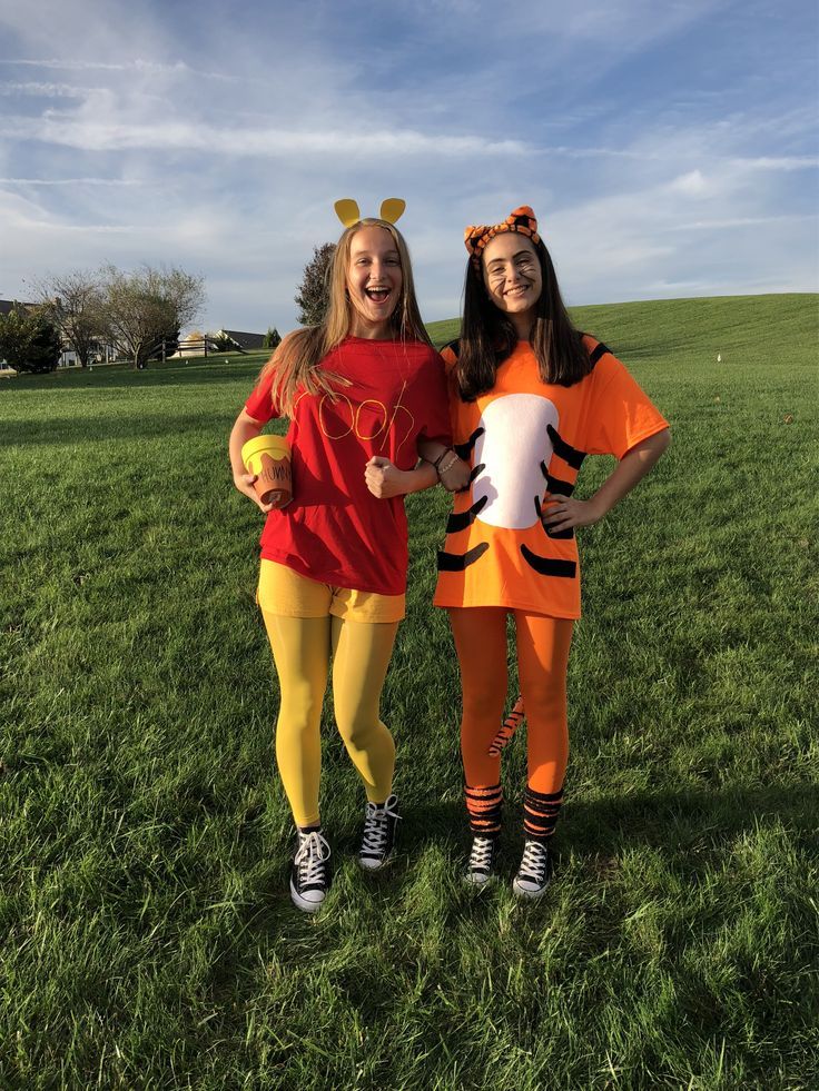 Two people dressed as Winnie the Pooh and Tigger in a grassy field, with a honey pot and painted tiger stripes
