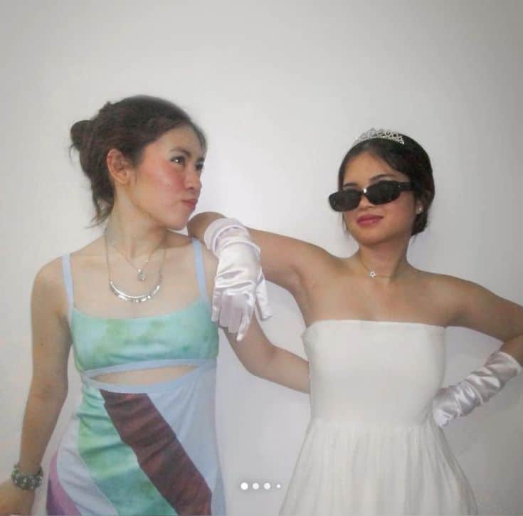 Two people dressed as Jenna from 13 Going on 30 in a printed cutout slip dress and Princess Mia in a white dress with a tiara and long gloves