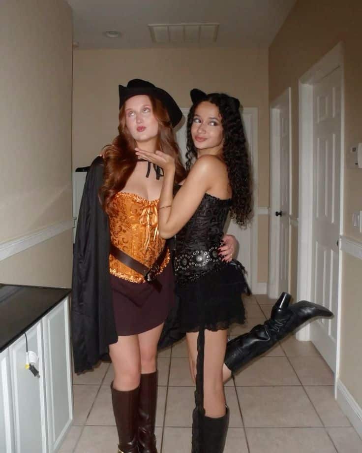 Two people dressed as Puss in Boots in an orange corset and hat and Kitty Softpaws in black with cat ears and a tail