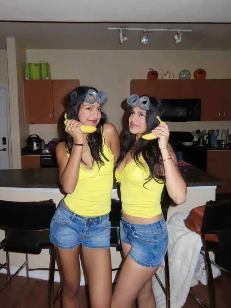 Two people dressed as Minions in yellow tops with goggle headbands, holding bananas