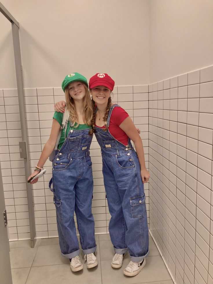 Two people as Mario and Luigi in denim dungarees with red and green letter caps