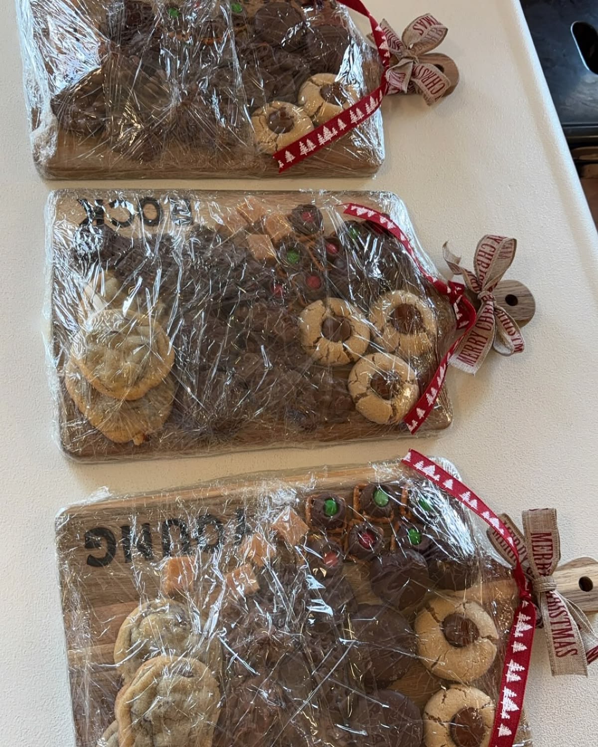 Wooden chopping boards of assorted homemade cookies and treats wrapped in cling film with Christmas ribbon