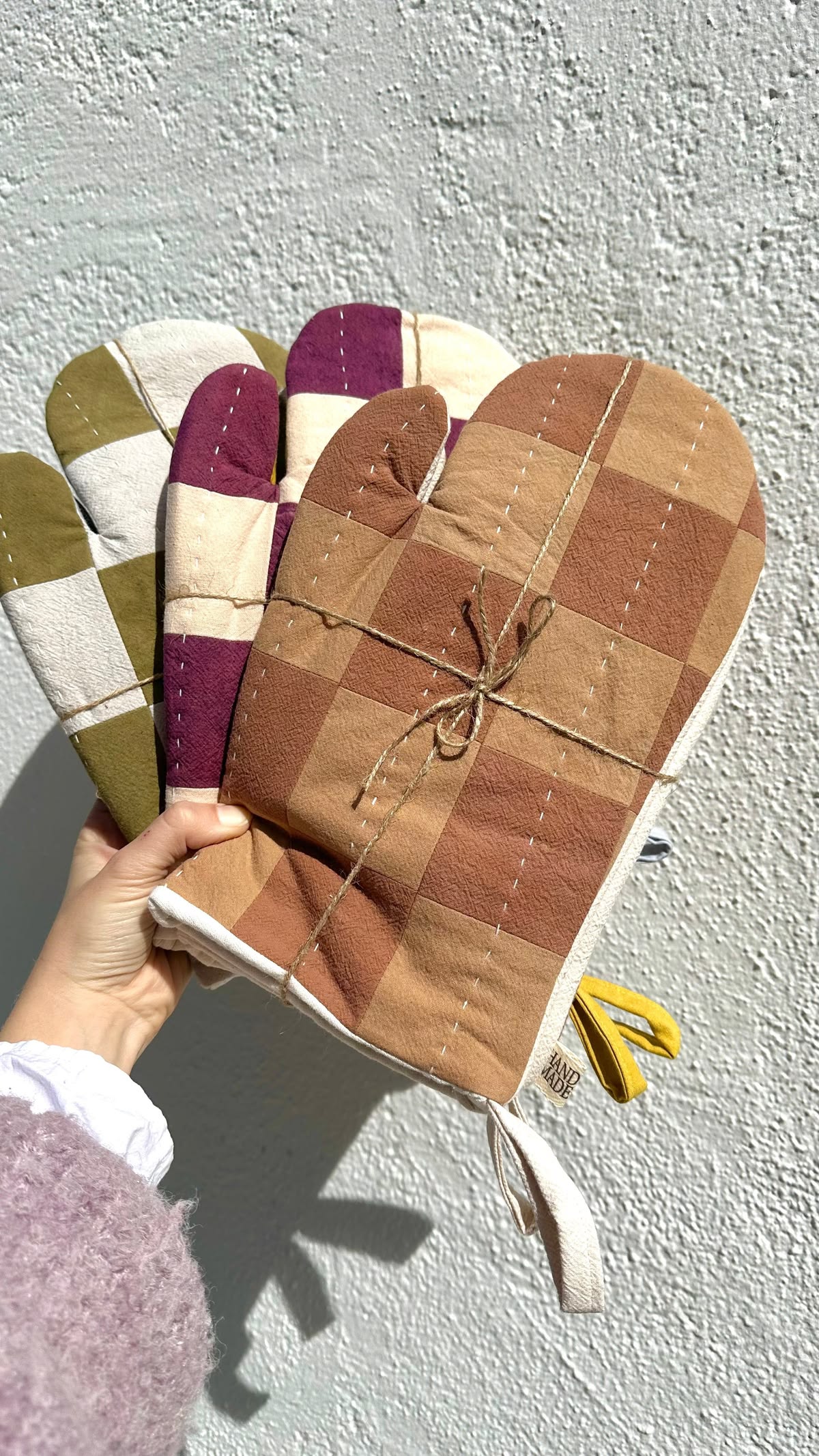 Quilted patchwork oven mitts in olive, plum and terracotta with visible hand stitching