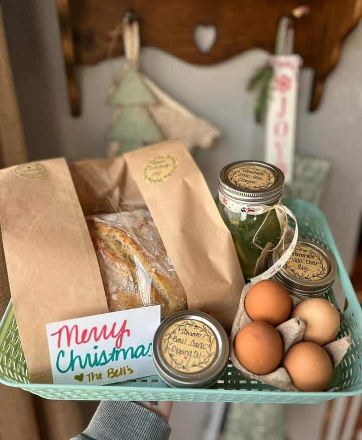 Gift basket with a loaf of bread in a paper bag, fresh eggs and small labelled jars of homemade goods