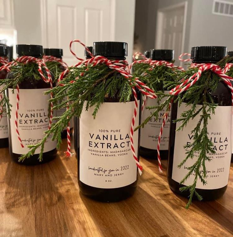 Amber bottles of homemade vanilla extract with printed labels, greenery and red and white twine