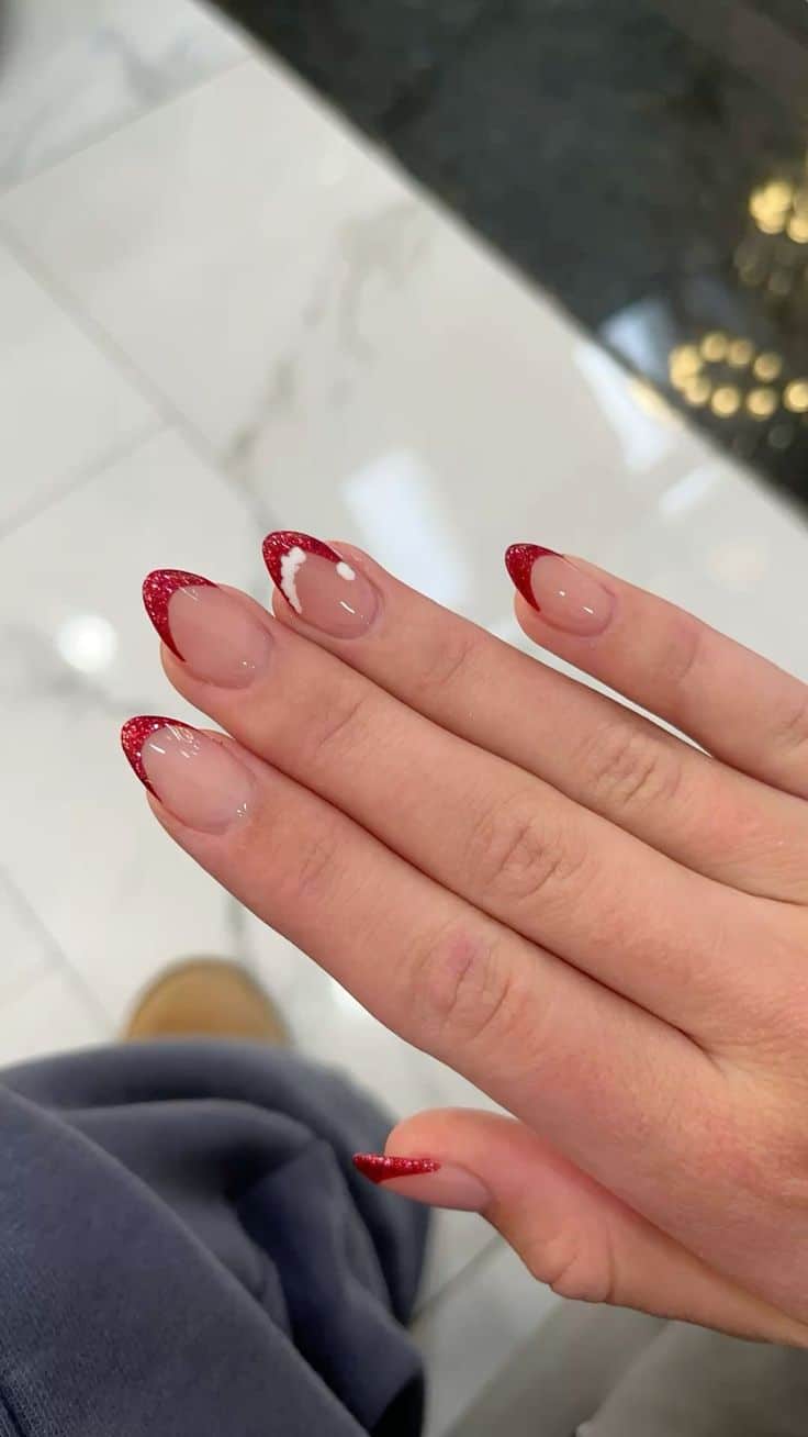Christmas nail ideas with red glitter French tips and a Santa hat accent