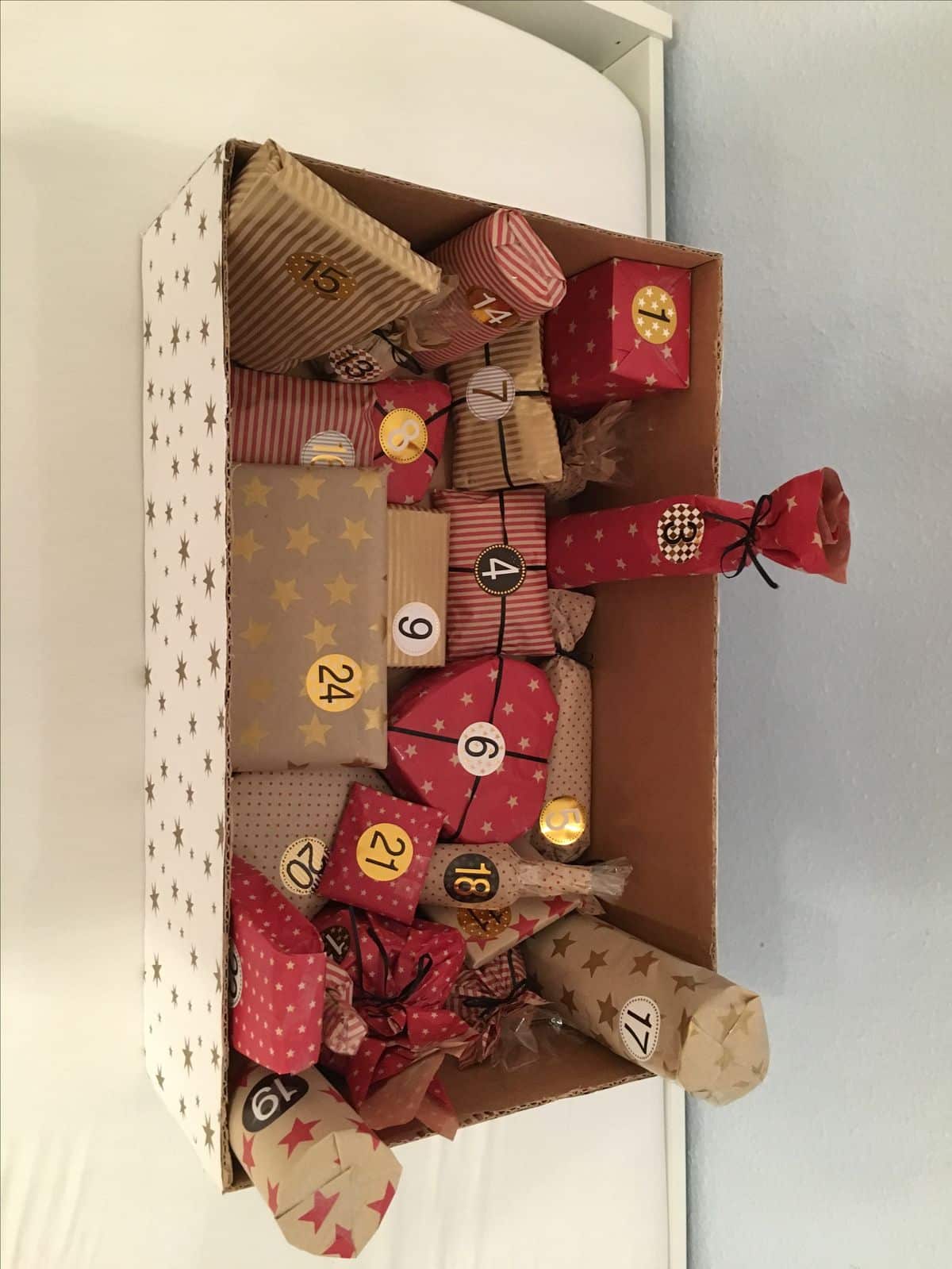 Box covered in gold star paper filled with red and kraft wrapped advent gifts with number stickers