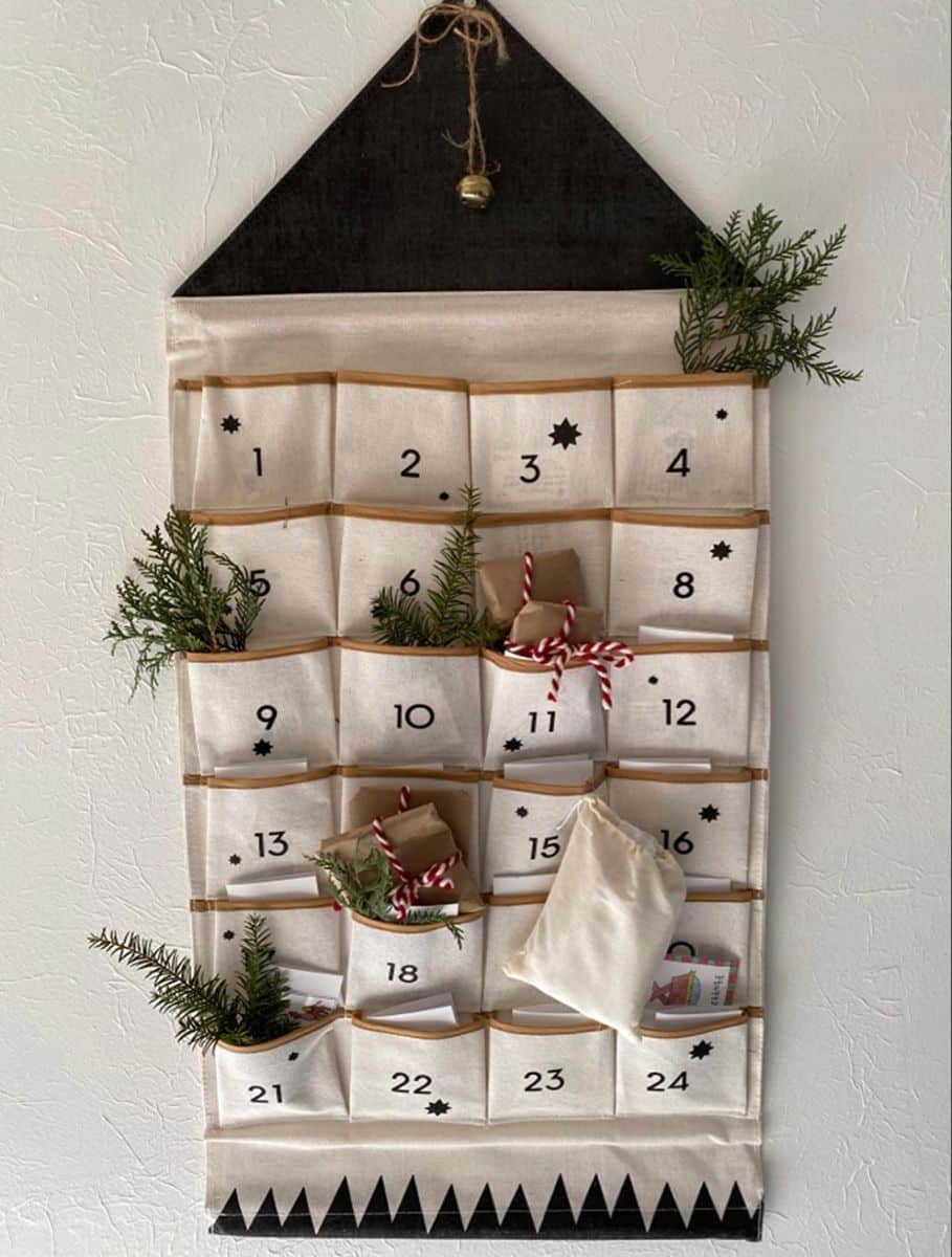 Canvas pocket advent calendar shaped like a house with a black roof, greenery and kraft parcels