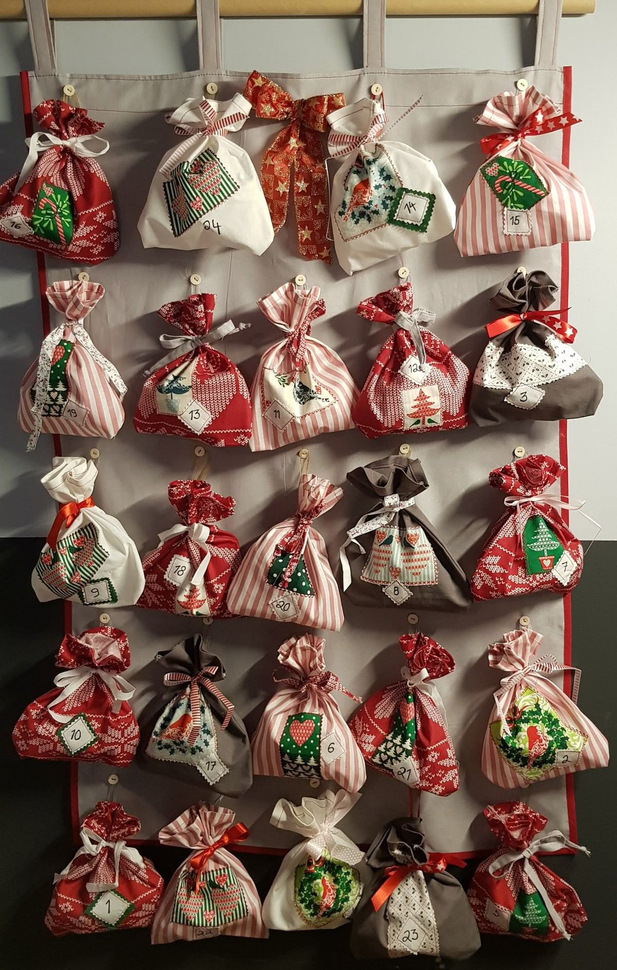 Red, white and grey fabric drawstring bags buttoned to a grey panel as a sewn advent calendar