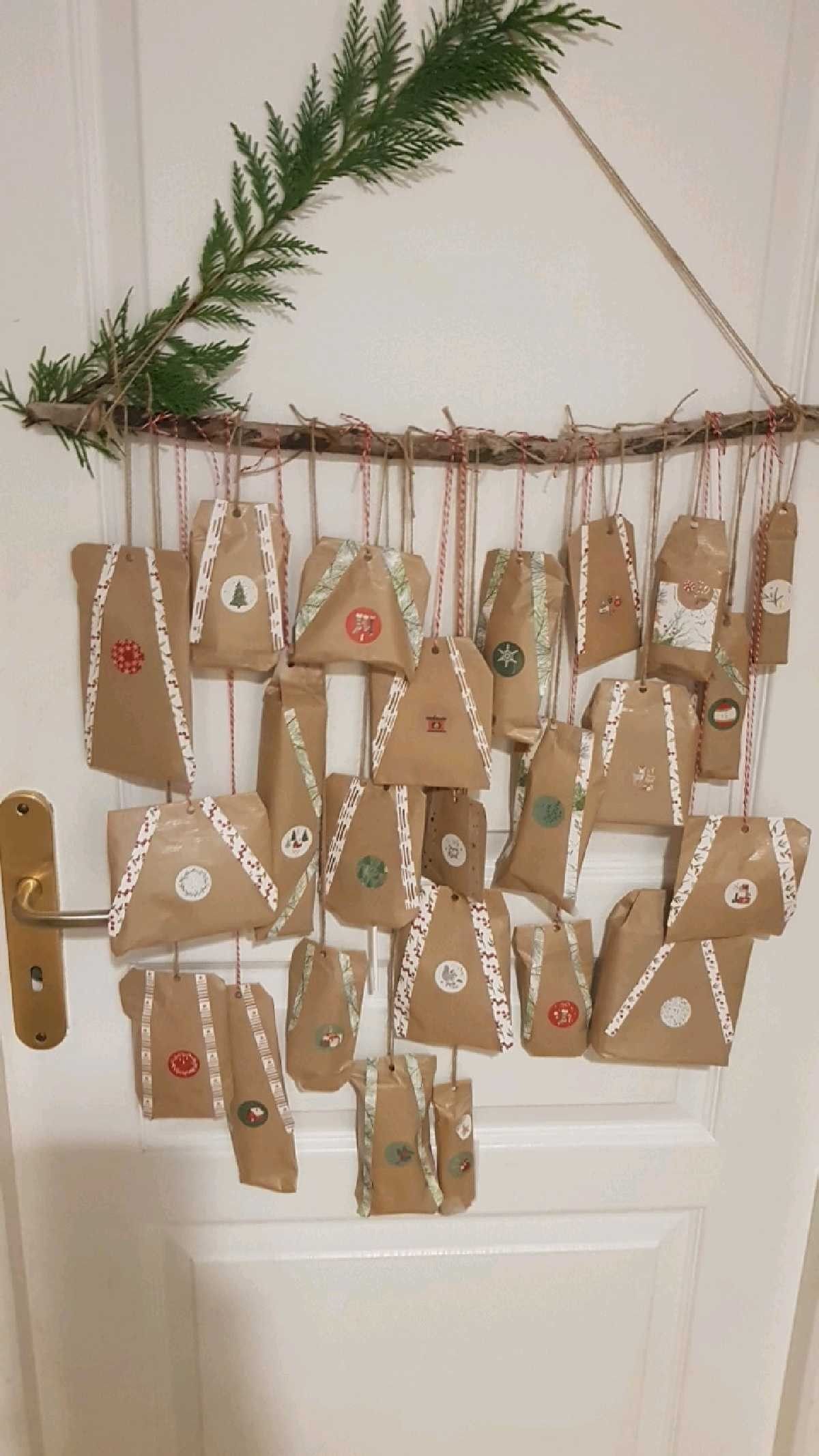 Branch hung on a white door with kraft paper advent parcels, washi tape and Christmas stickers