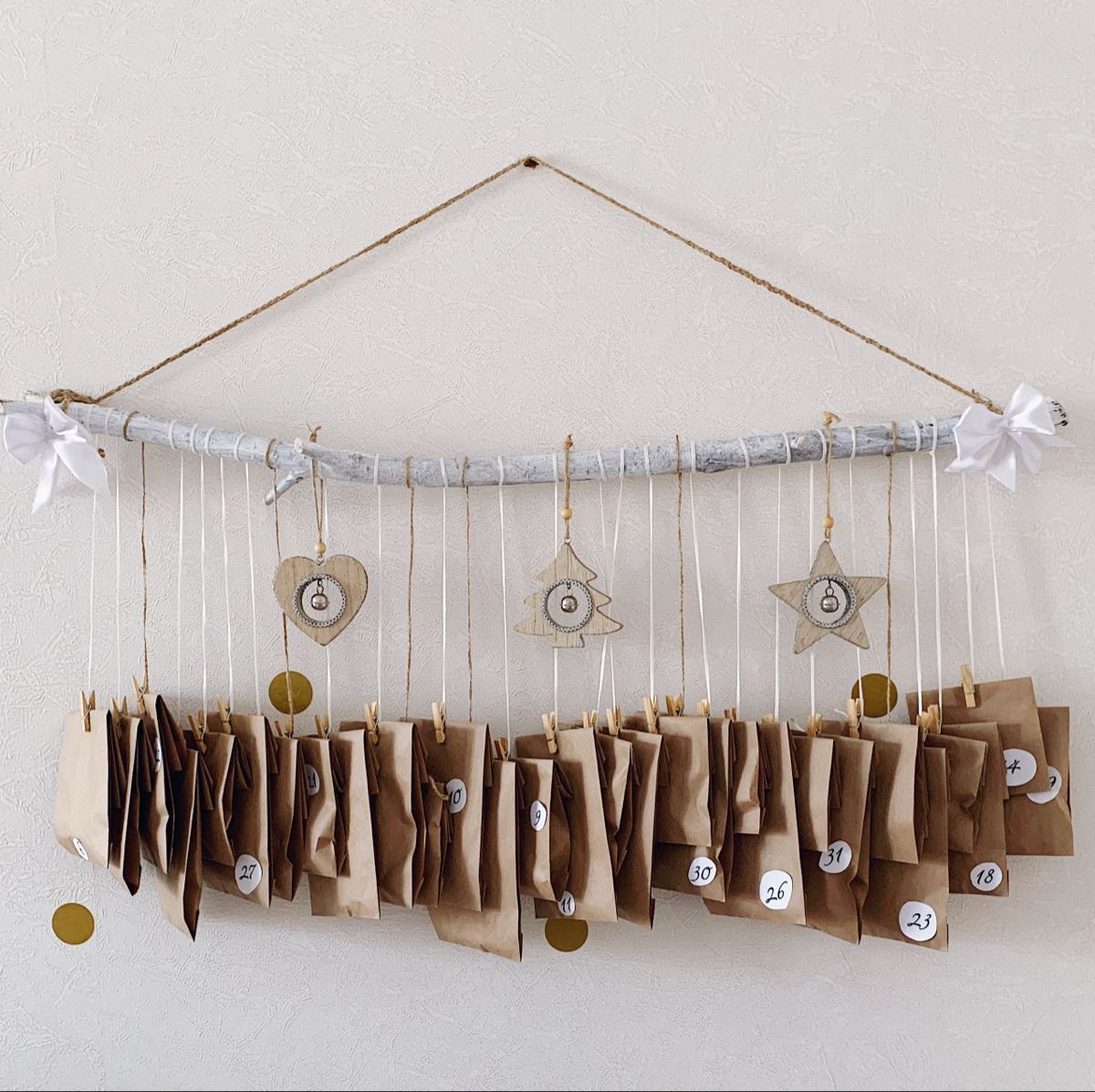 Whitewashed branch advent calendar with kraft envelopes on mini pegs and wooden heart, tree and star ornaments