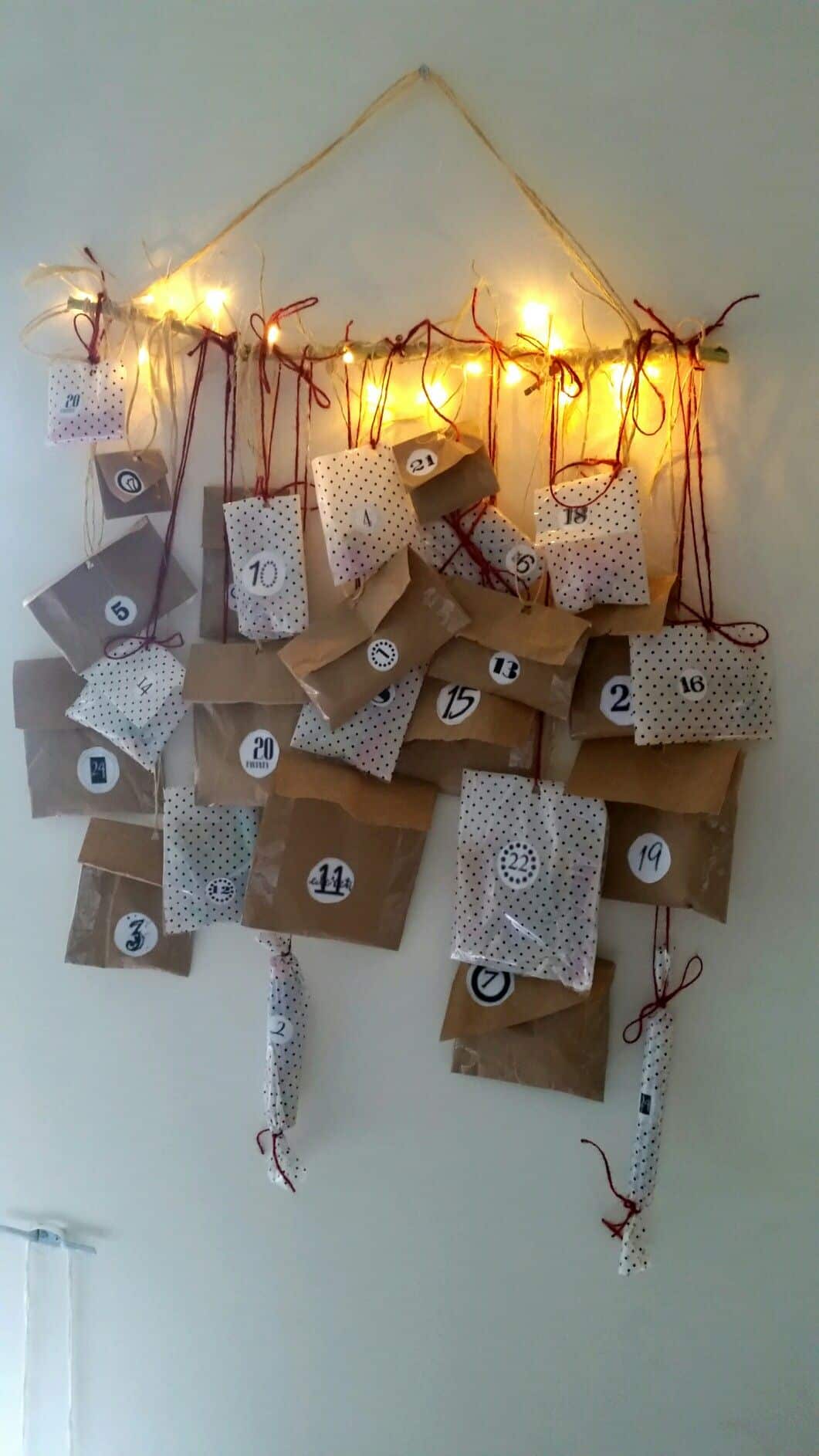 Branch wrapped in fairy lights with kraft and polka dot paper bags hanging as an advent calendar