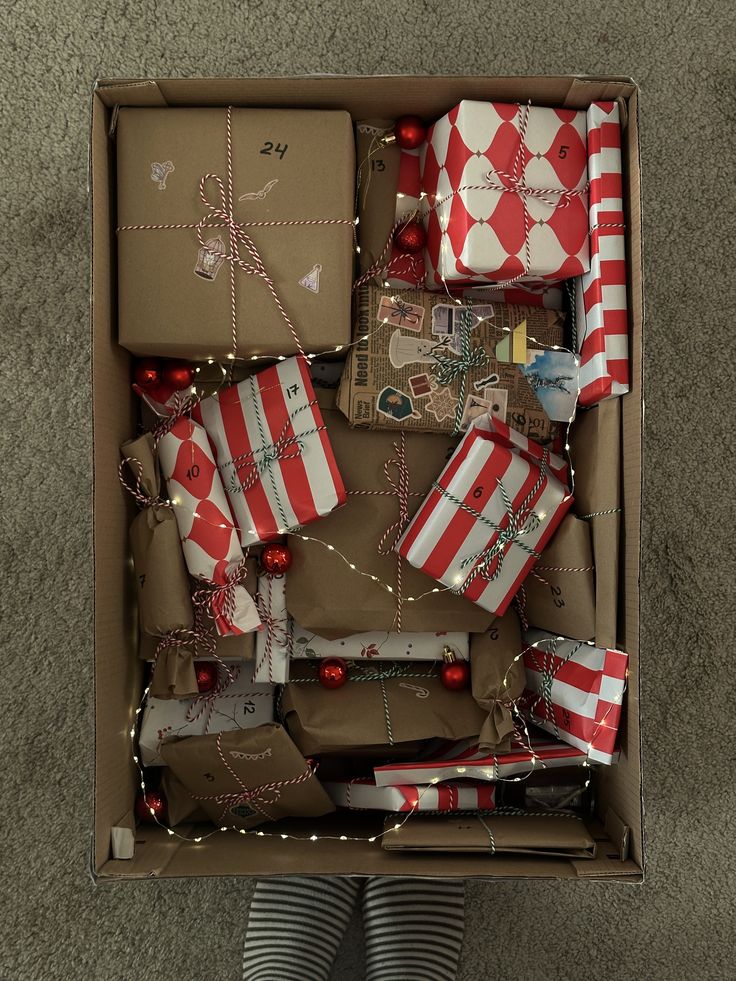 Cardboard box filled with red and white striped and kraft wrapped advent gifts, fairy lights and baubles