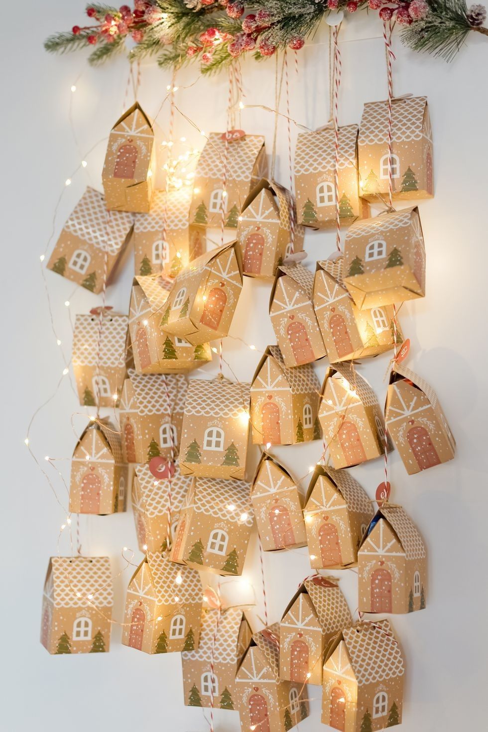 Kraft gingerbread house gift boxes hanging on twine with fairy lights as a DIY advent calendar