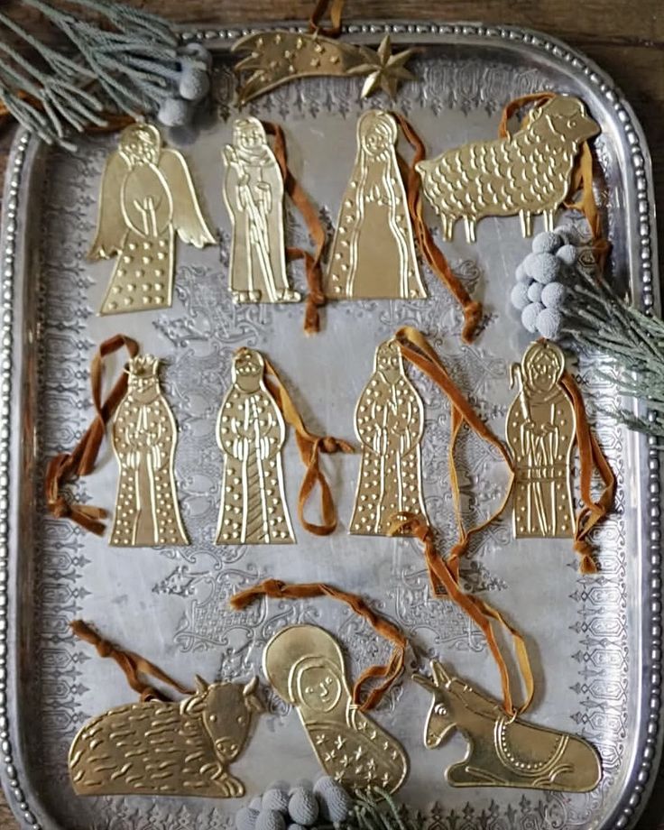 Embossed gold brass nativity ornaments with rust velvet ribbon hangers on a silver tray