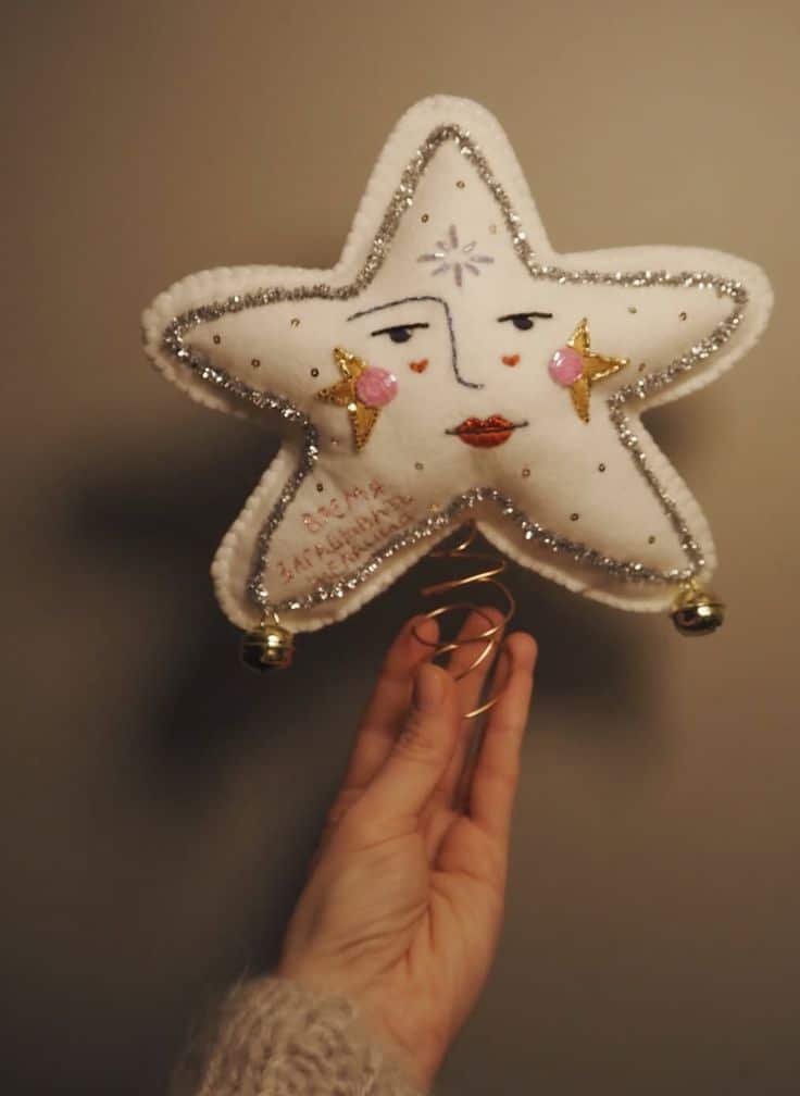 White felt star tree topper with an embroidered face, silver tinsel trim and small bells