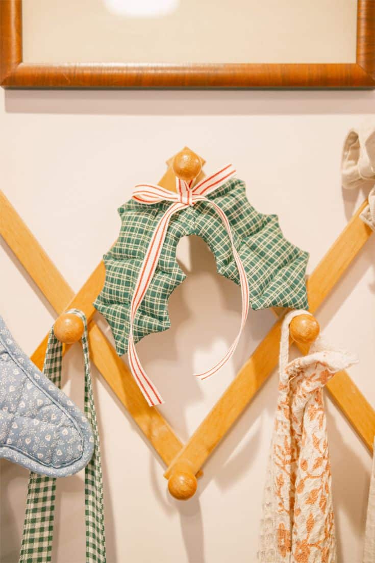 Puffy green plaid fabric holly wreath ornament with a red and white striped ribbon bow