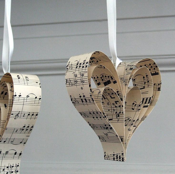 Three-dimensional heart ornaments made from folded strips of sheet music hanging on white ribbon